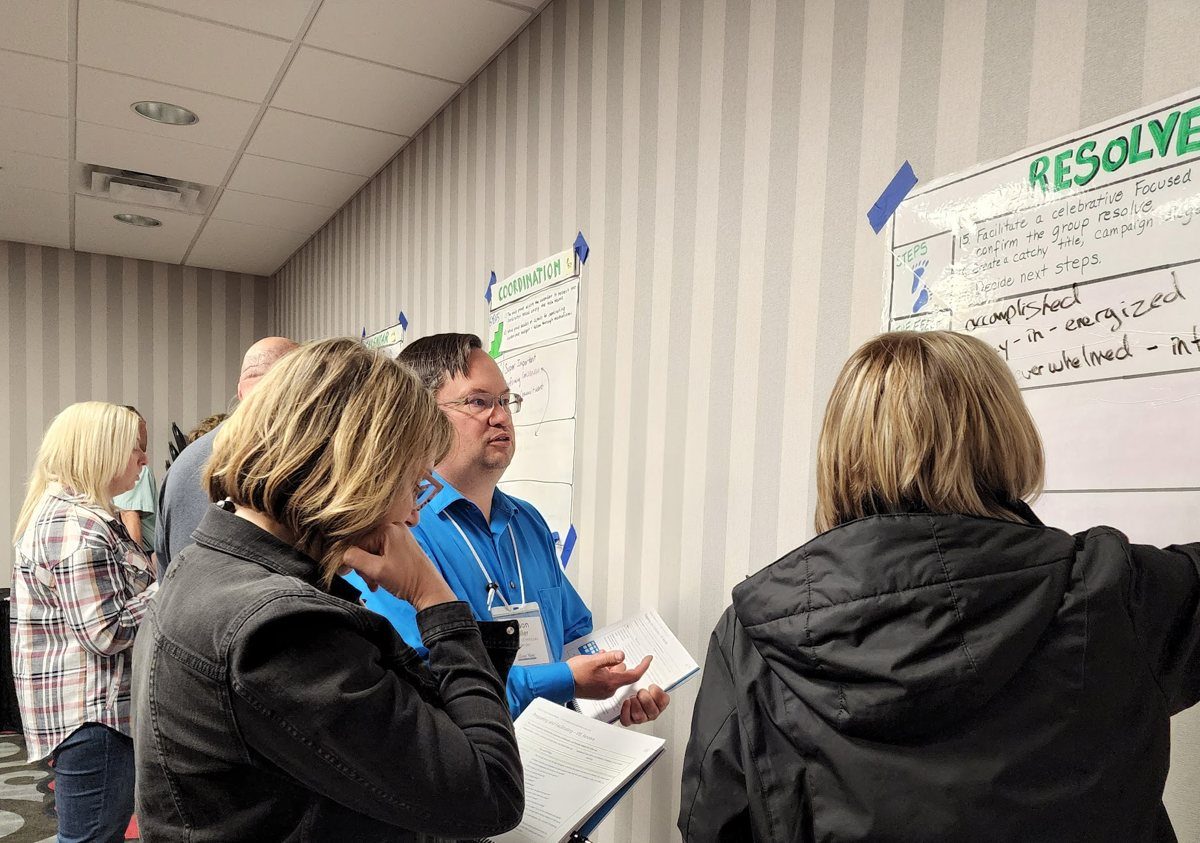 Course participants working together at a wall chart, one writing while others discuss
